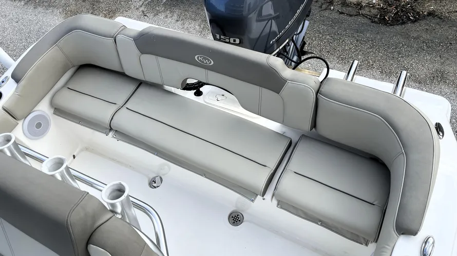 The rear seating area of a boat, featuring a cushioned bench seat in light gray with a backrest for added comfort. The seating is designed to provide ample space for passengers to sit comfortably at the stern of the boat. Behind the seating area, a Yamaha 150 outboard motor is visible. The area includes rod holders on the side and stainless steel cup holders. The layout is practical, offering both comfort and functionality for family outings or fishing trips.