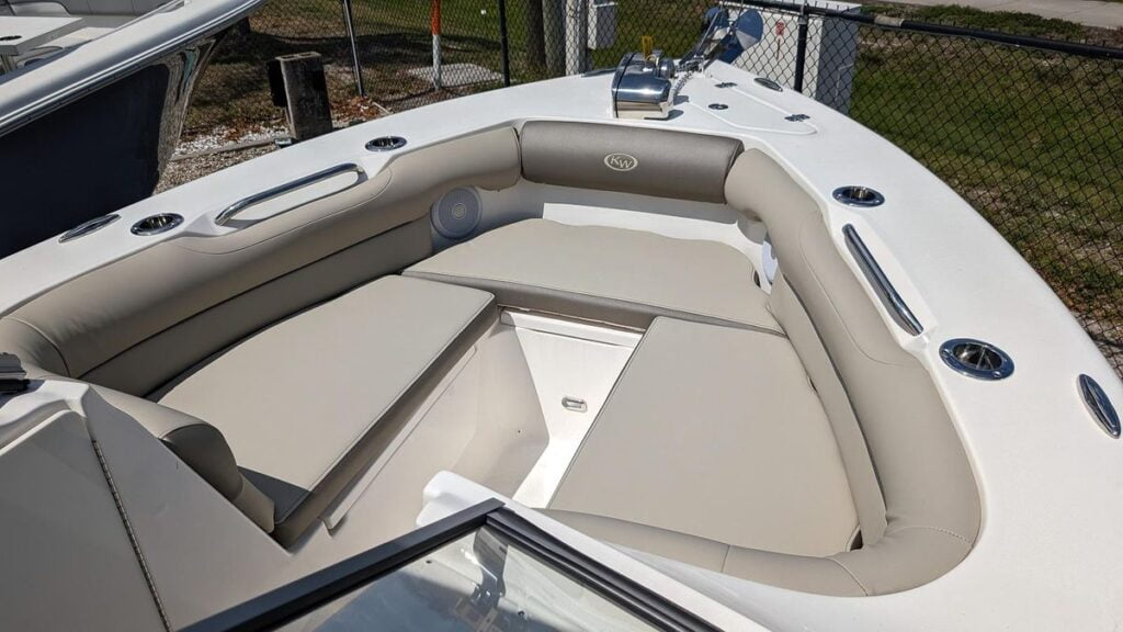 The bow seating area of a Key West 239 DFS dual console boat, featuring plush, light gray cushions and a wrap-around seating layout. The cushions provide ample comfort for passengers to relax, and the area is equipped with stainless steel cup holders and grab rails for convenience and safety. A speaker is visible on the side, offering entertainment options. The design is spacious, allowing multiple passengers to enjoy the front of the boat while cruising or anchored.