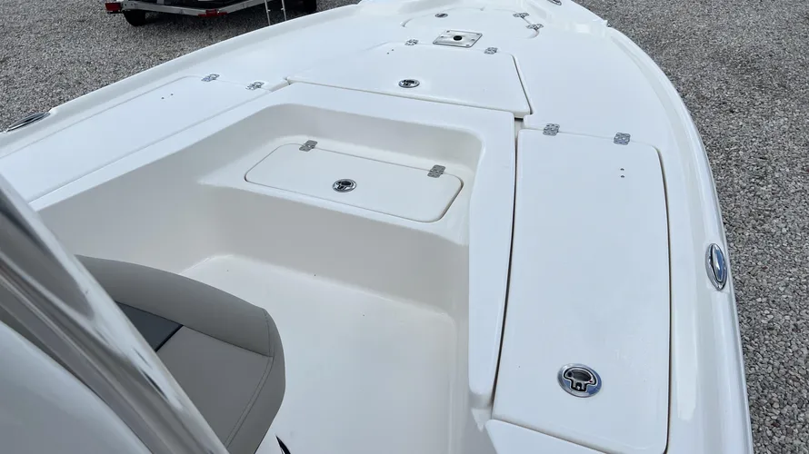 The bow area of a boat featuring multiple storage compartments with secure latches. The clean, white deck includes a recessed area for seating or standing, with the compartments designed for easy access to store gear and equipment. The surface is smooth, and the hatches are flush with the deck, creating an organized and functional space. The boat's deck provides ample room for fishing or relaxing, and the layout is practical for both cruising and fishing trips.