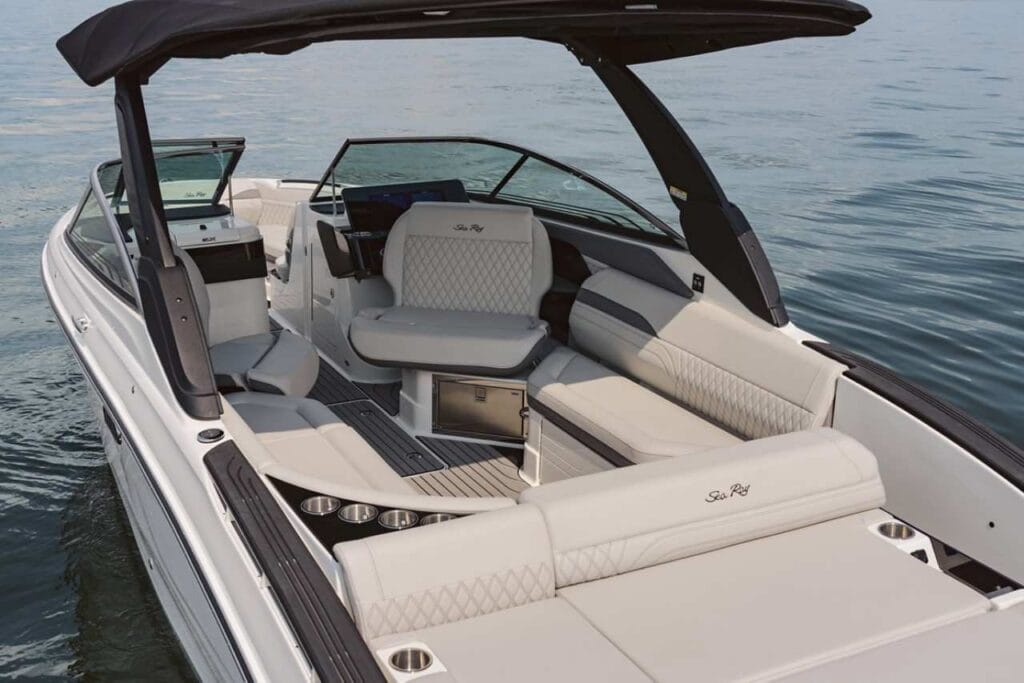 The interior of a luxury Sea Ray bowrider boat featuring sleek white upholstery with quilted detailing, spacious L-shaped seating, and a well-designed lounging area. The open layout includes cupholders and a shaded canopy, perfect for relaxing on the water.